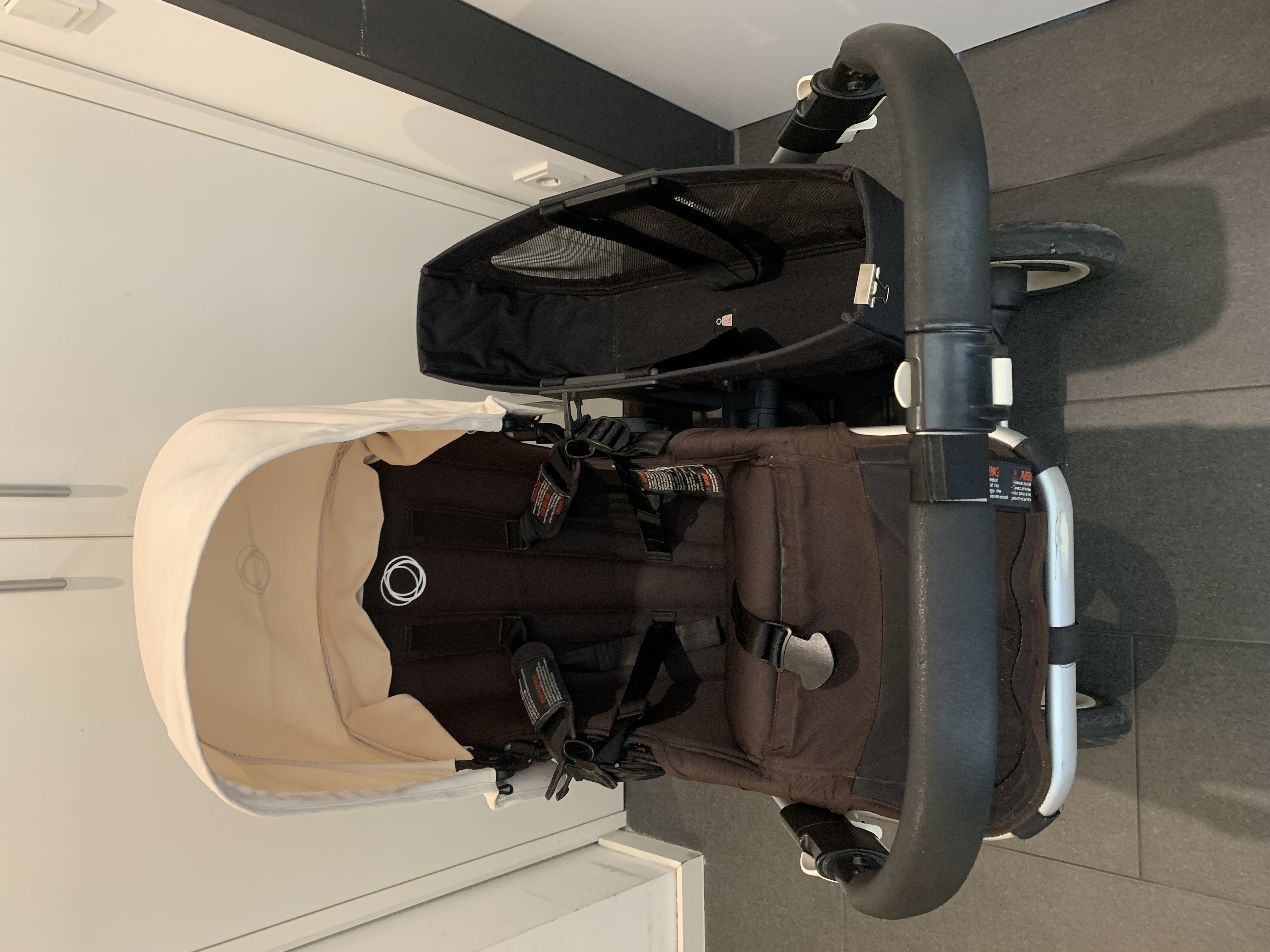 Siège Bugaboo Donkey Duo vu de derrière, avec capote, harnais, guidon et panier latéral visibles.