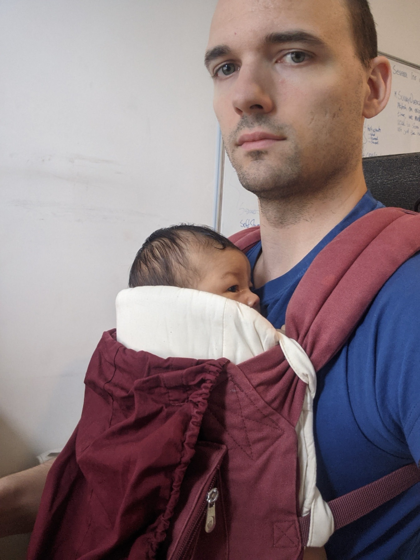 Mia figlia neonata appoggiata a me in un marsupio strutturato bordeaux con un inserto chiaro che sostiene testa e collo.