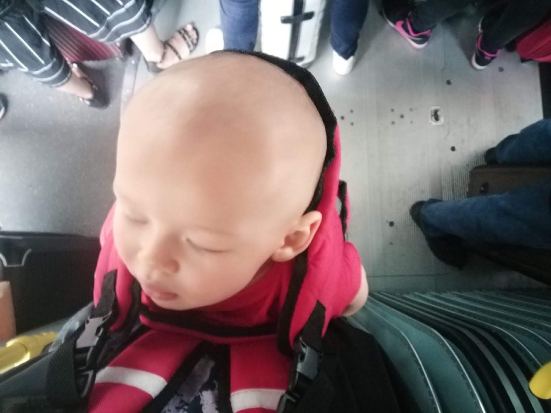 Mio figlio piccolo addormentato nel marsupio rosso su mezzi pubblici affollati, dove ci sarebbe stato poco spazio per gestire un passeggino.