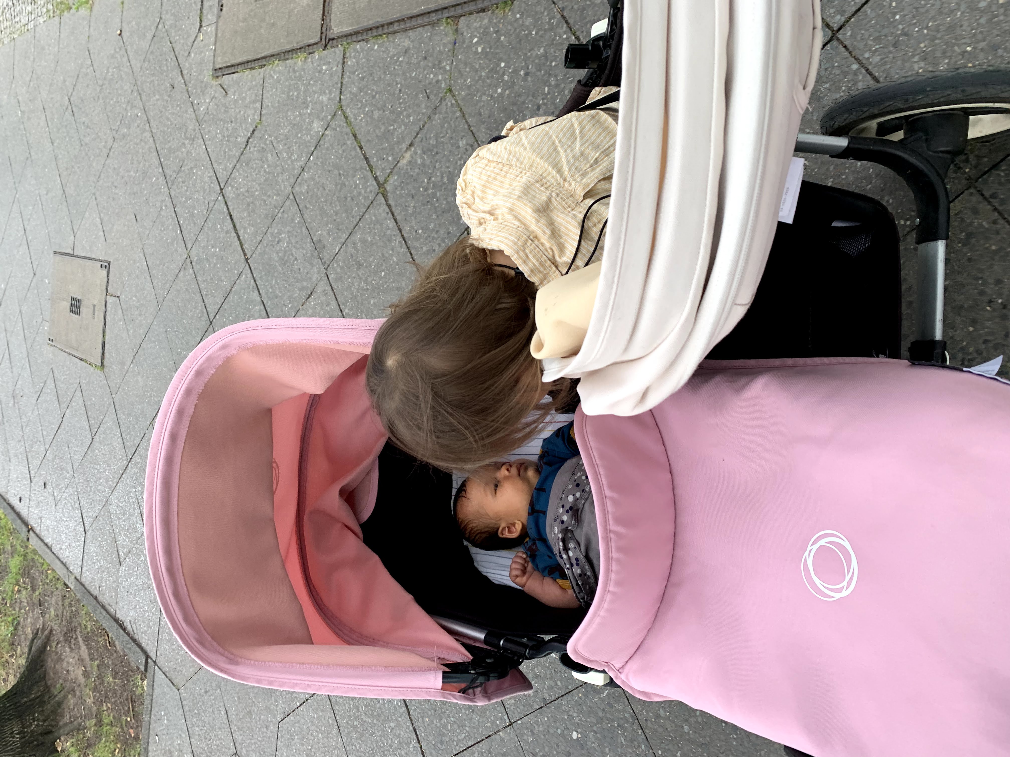 我家儿子坐在 Bugaboo Donkey 5 的双人模式座椅里，看着躺在睡篮里的妹妹。