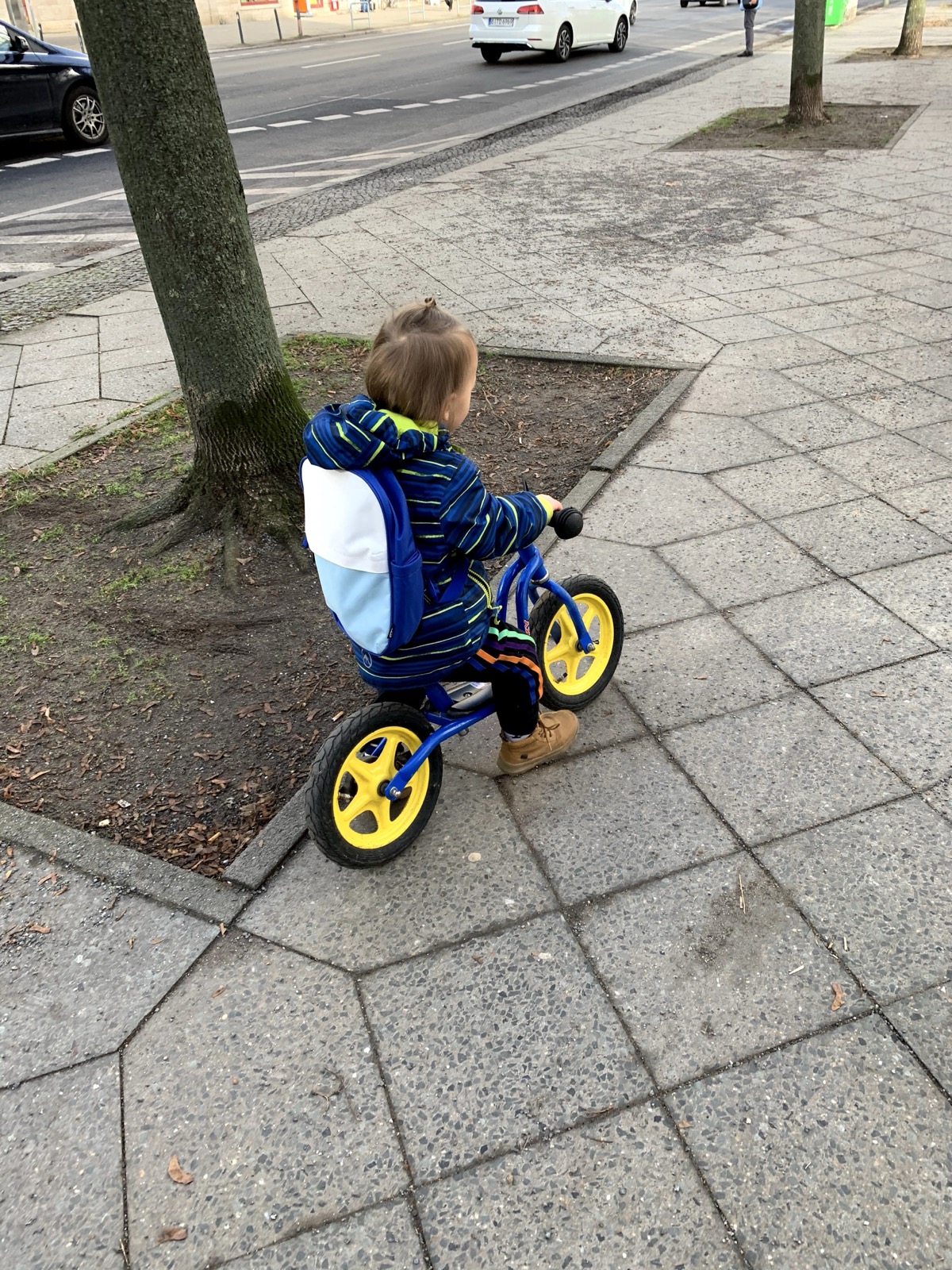 Mein Sohn fährt mit dem Laufrad an einem Stadtgehweg entlang.