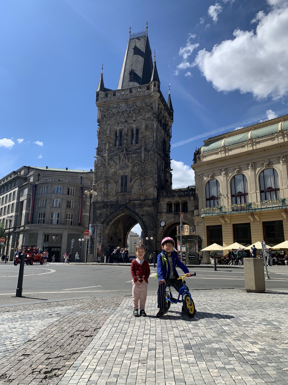 Meine Kinder stehen mit dem Laufrad auf einem Kopfsteinpflasterplatz in Prag.