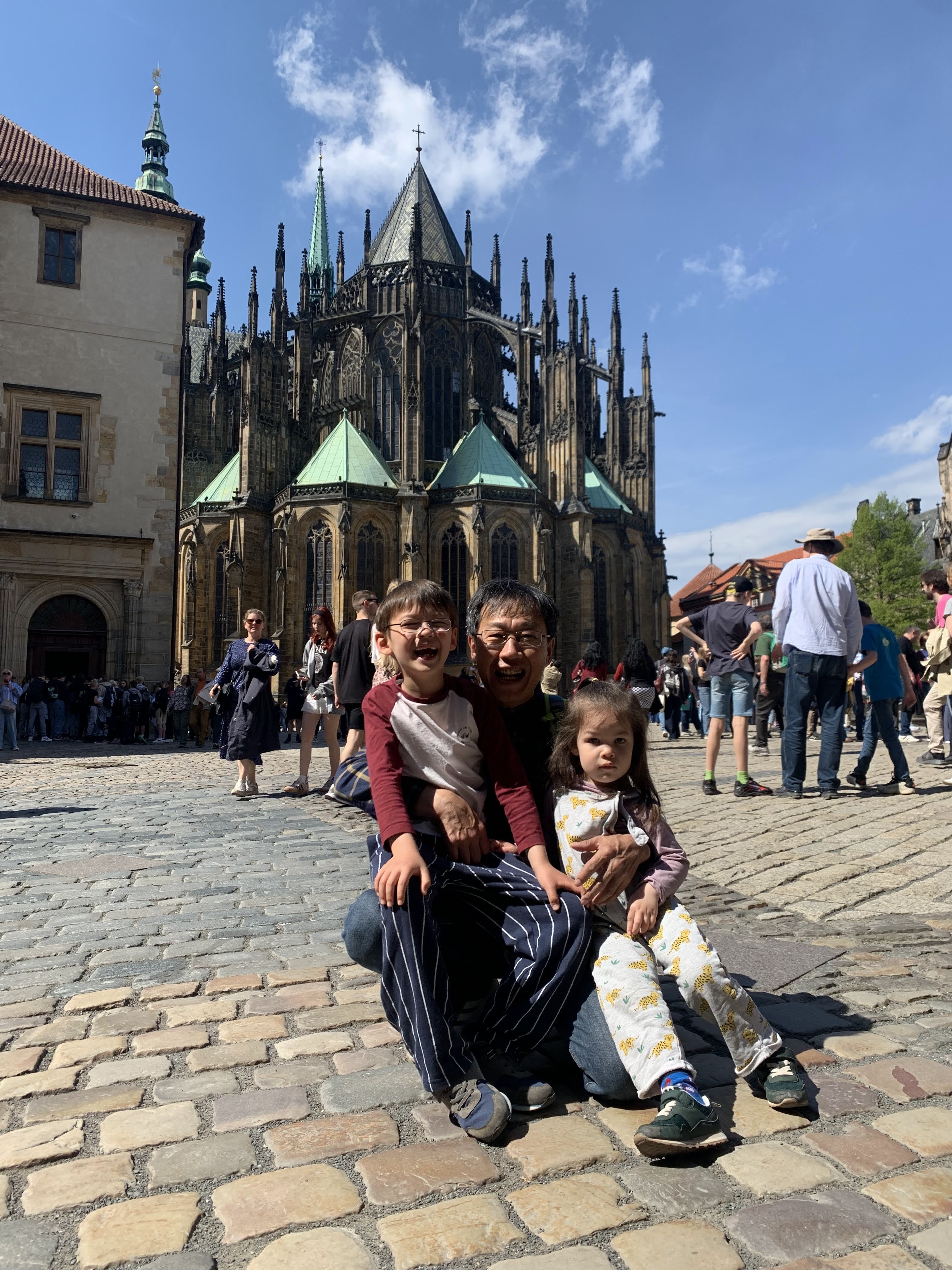 Our family sitting outside St. Vitus Cathedral during a sunny Prague city walk with children and a grandparent.