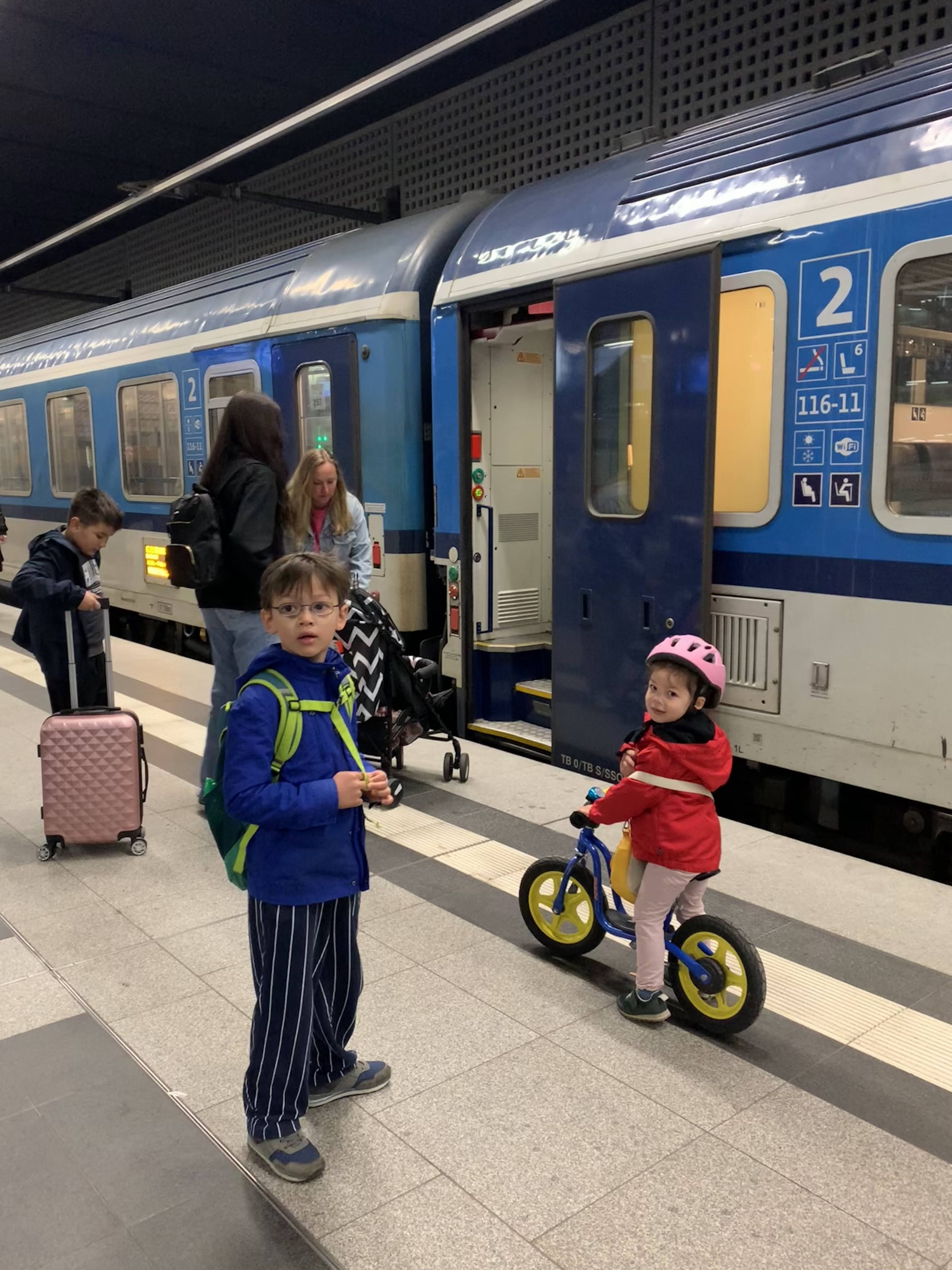 The children standing by the Prague train before the city part of the trip, with the balance bike ready for station transfers.