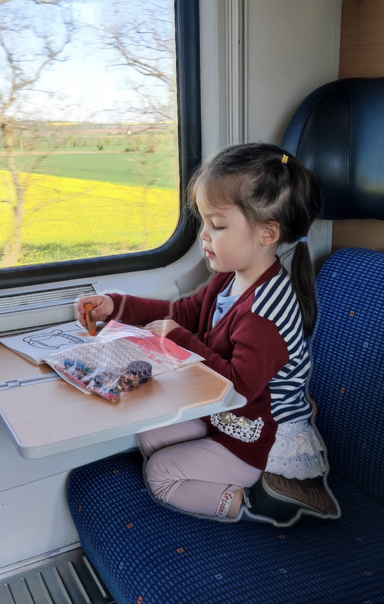 Our daughter drawing at the train table while the Berlin to Prague route passes spring fields outside the window.