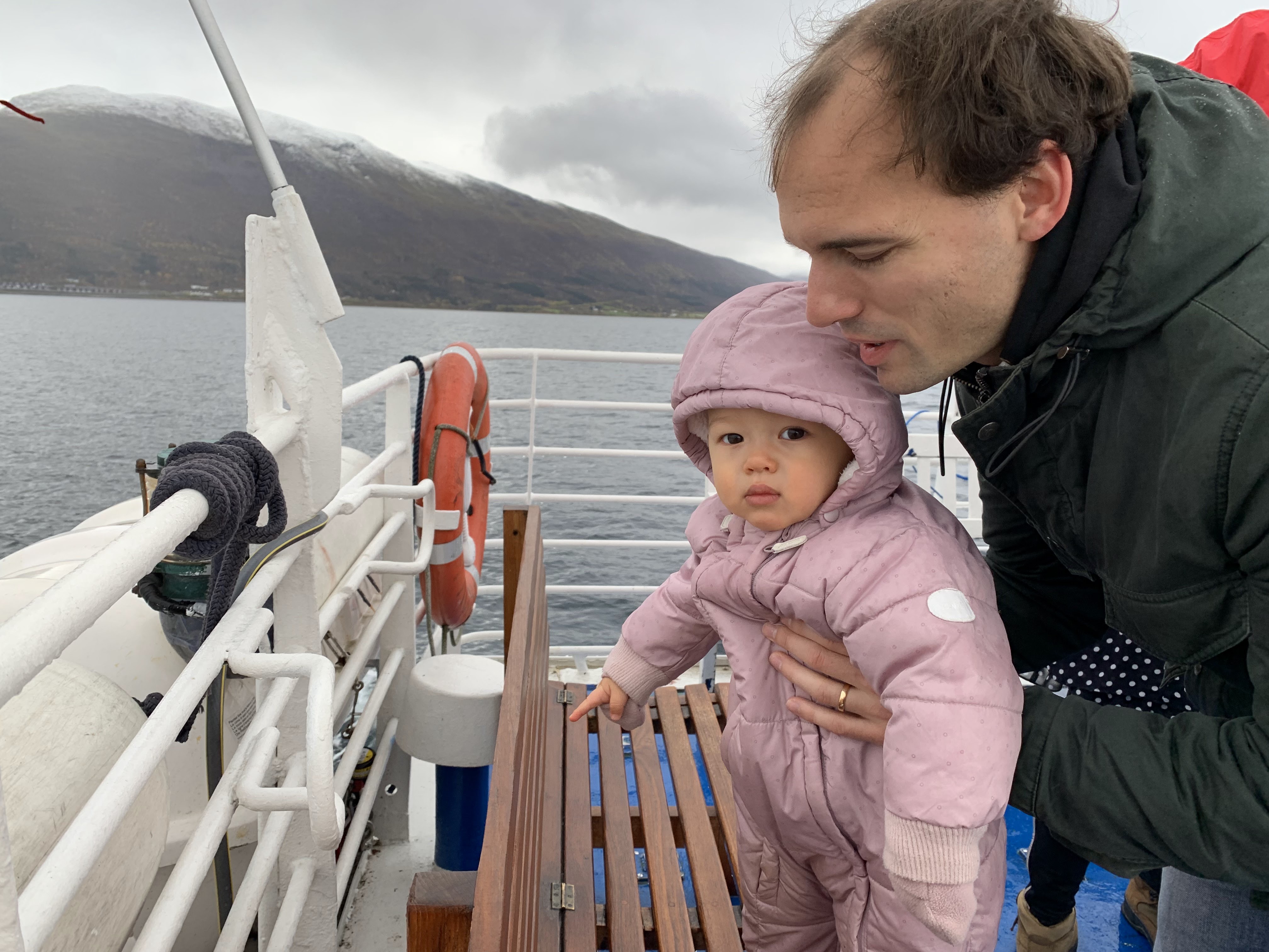 Ich halte meinen Sohn auf dem Deck unserer Fjord-Bootstour ab Tromso, mit Bergen und kaltem Wasser hinter uns.